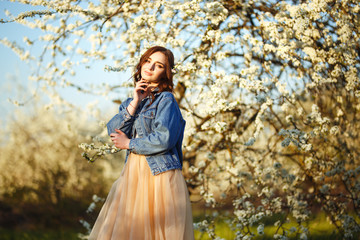 Portrait of a beautiful bride. Wedding concept. Stylish wedding. Great sunset light. She is wearing a blue denim jacket, dress. Spring blooming garden.