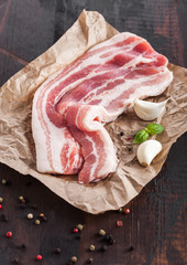 Raw fresh smoked pork bacon slices on butchers paper on dark wooden board with garlic basil.