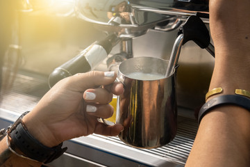 Barista pouring milk from coffee machine in milk jar to prepare latte foam in coffee shop close up