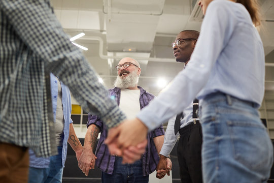 Mid section view at of people holding hands standing in circle during therapy session in support group, copy space