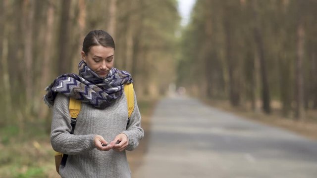 Young hitchhiking woman on road smoking cigarette 