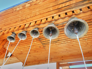 Bronze metal bells suspended from wooden boards of gold color against a blue sky. Religion. Attributes of religion. Old style. Bells and ropes. Bell ringing. Buddhism and Christianity.