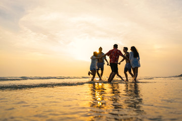 A group of male and female friends who play fun on the sea beach amid the sunset. - obrazy, fototapety, plakaty