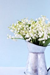 Lilies of the valley a bouquet in an iron jug on a blue background. place for text. copy space.