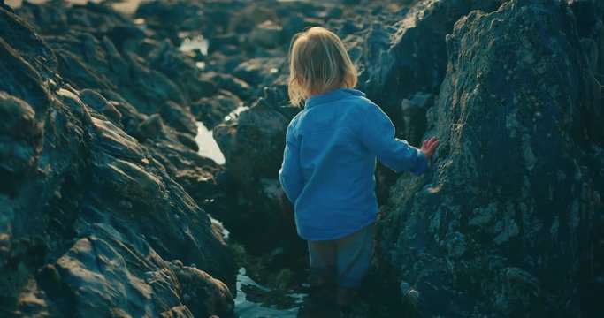 Little toddler walking on the beach at sunset between rocks