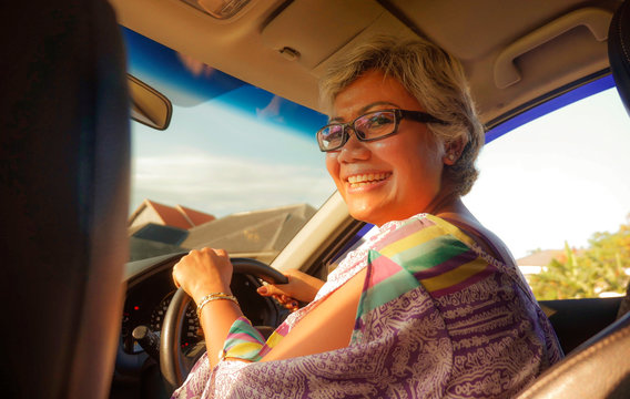 lifestyle Summer portrait of middle aged happy and attractive classy Asian Indonesian woman driving left hand car smiling cheerful and free on a sunny day