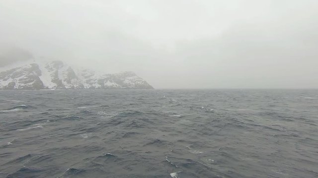 Ship in rough sea in old and windy weather POV from deck of ship with view of snow covered coastline