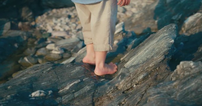Little toddler walking barefoot on rocks at the beach