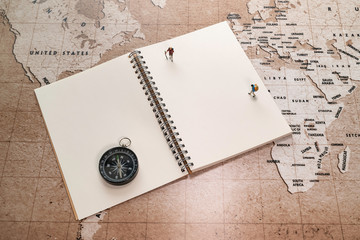Two small miniatures on white notebook with compass on world map