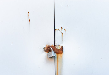 Locked simple metal padlock hanging on rusted hasp on metal doors.
