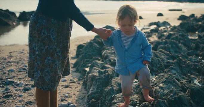 Little toddler walking with his mother on stony beach