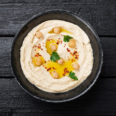 Hummus, chickpea dip, with spices in a black plate on black wooden background. 