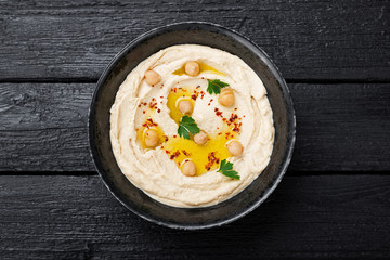 Hummus, chickpea dip, with spices in a black plate on black wooden background. 