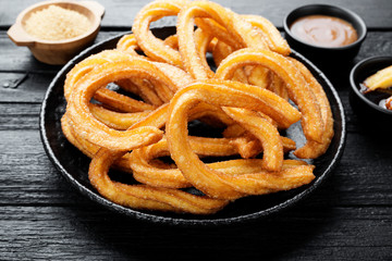 Churros with sugar and chocolate sauce on black wooden background.
