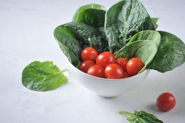 Bowl with spinach leaves and cherry tomatoes. The concept of a healthy diet. Close-up. Light background. 