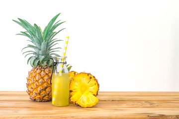 Bottles of a pineapple juice with sliced pineapple fruit on wooden table with white background ,...