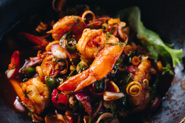 Spicy seafood salad in black plate on wooden table