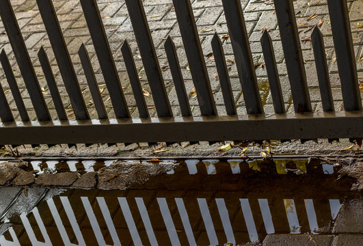 Metal security fencing reflected in a rain puddle forming patterns image with copy space in landscape format
