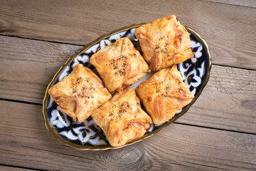 samosa with potatoes, meat and pumpkin on plate with traditional Uzbek ornament on wooden background, cooked in the tandoor. National Uzbek pastries. Flat lay.Top view. Street fast food. Rustic style