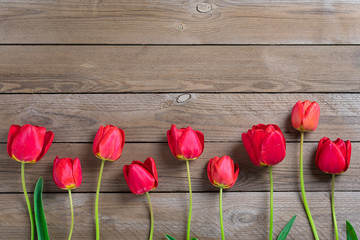 Fototapeta na wymiar Row of red tulips on wooden background with space for text, message. Mother's Day, Hello spring concept. Card. Flat lay. Top view. Rustic style. 