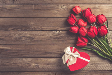 Row of red tulips and box  in shape of heart on wooden background with space for text, message. Mother's Day, Hello spring concept. Card. Flat lay. Top view. Rustic style. 
