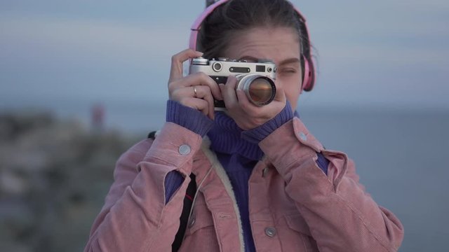 Girl in headphones takes a picture of the sea sunset on her vintage camera