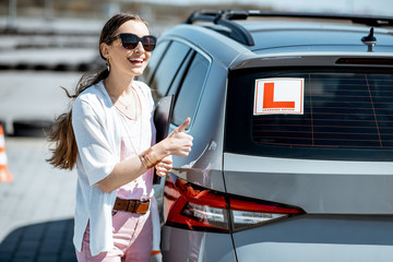 Portrait of a young female student standing near the learning car on the training ground at the...