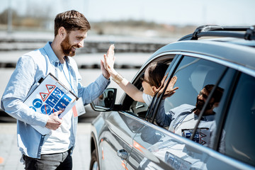 Instructor giving a five to a woman driver sitting in the car while learning to drive on the...