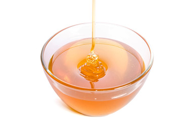 Pouring honey into a glass bowl on a white background