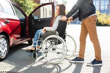 Obraz na płótnie Canvas Man With Her Disabled Wife Moving Towards Car