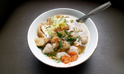 Indonesian traditional meatballs or bakso. Soup containing meatballs, noodles, fried tofu and cucumber pickles