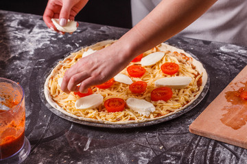 young woman in a gray aprong prepares a pizza margarita