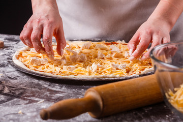 young woman in a gray aprons prepares a Hawaiian pizza