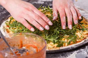 young woman in a gray aprong prepares a vegetarian pizza