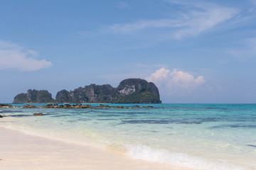 Fototapeta premium Blue sea and white sand with tropical mountains in the background