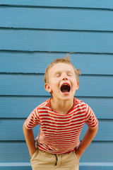 Cute little boy in striped T-shirt posing in front of blue house wall.