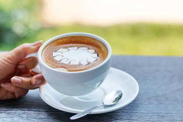 Hands are holding a cup of hot latte coffee on a natural blurred background.
