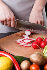 young woman in a gray apron cuts a radish