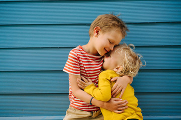 Outdoor portrait of big brother and his little sister against blue house wall
