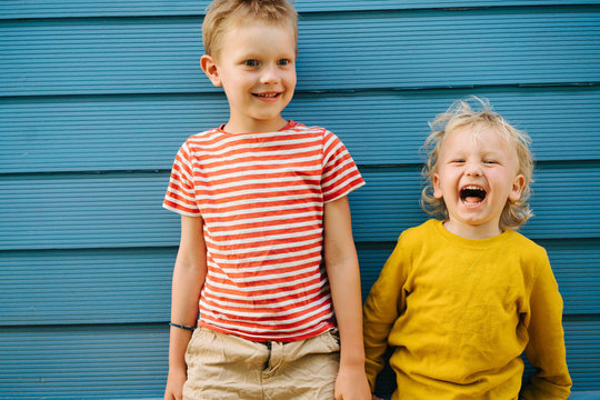 Outdoor Portrait Of Big Brother And His Little Sister Against Blue House Wall