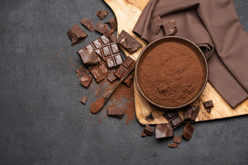 Dark Chocolate chunks and cocoa powder in wooden bowl on dark concrete background