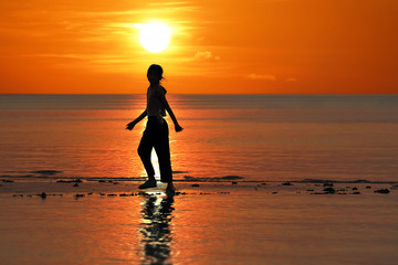 Fototapeta na wymiar Silhouette of single Asian girl enjoying herself during sunset on the beach red sky