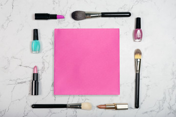 Flat lay of cosmetic products with blank pink paper card on white marble background. Makeup mockup