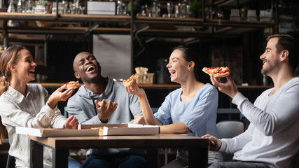 Multiracial friends laughing eating pizza gathered together in pizzeria