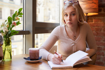 A woman sitting in a cafe at a large panoramic window. A young girl writes important things in a...