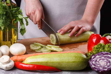 young woman in a gray apron cuts a cucumber