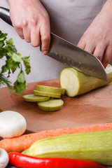 young woman in a gray apron cuts a zucchini