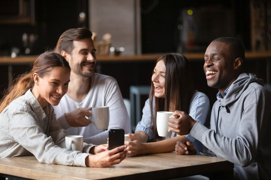 Four diverse friends having fun use gadget sitting in cafe