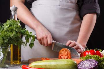 young woman slicing a tomato in a gray apron