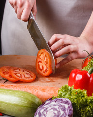 young woman slicing a tomato in a gray apron